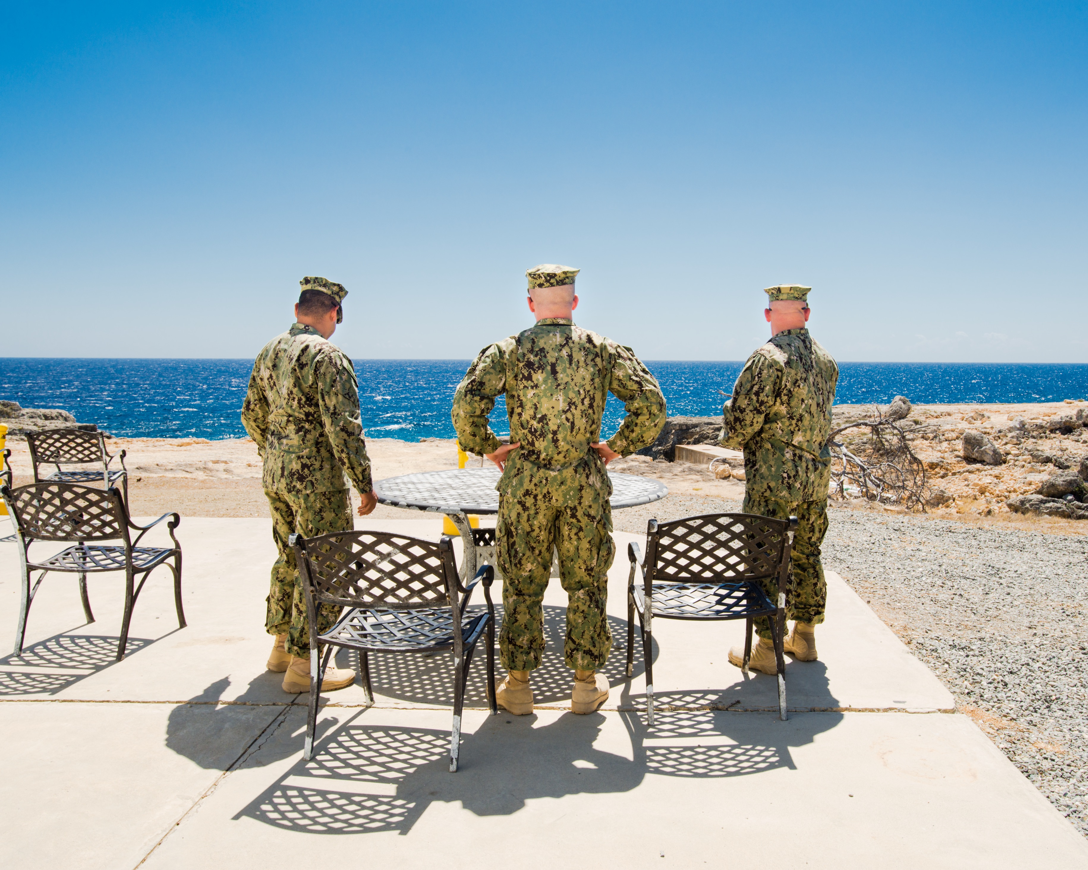 Zigarettenpause, Camp America, 2014. (c) Debi Cornwall Drei Soldaten bei der Zigarettenpause, von hinten fotografiert, mit Blick aufs Meer. (c) Debi Cornwal