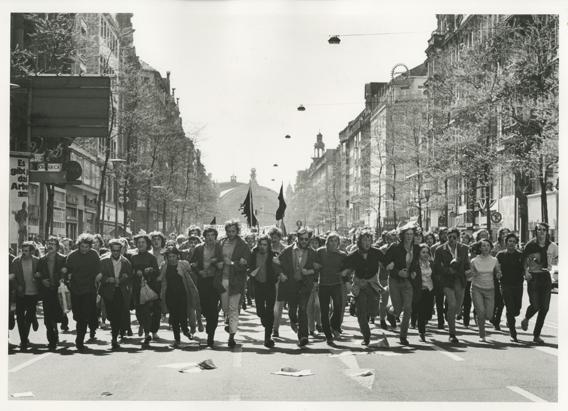 Schwarz-weiße Fotografie einer Straße in Frankfurt. Eine Reihe von Demonstrierenden läuft auf die Fotografin zu. Foto: Barbara Klemm